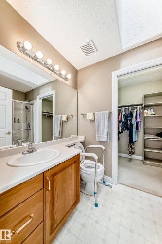 Bathroom featuring a wood-finish vanity with a white countertop and integrated sink, full-width mirror, and a built-in closet with shelving - 29 929 Picard Drive, Edmonton, AB - Indoor Photo Showing Bathroom