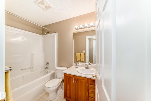 Full bathroom featuring a white tub and shower combination with a single-handle faucet, a white toilet, a wood-finish vanity with a white countertop and integrated sink, and an overhead vanity light fixture - 29 929 Picard Drive, Edmonton, AB - Indoor Photo Showing Bathroom