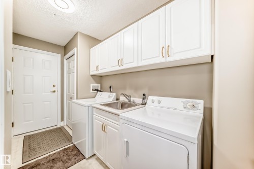 Dedicated laundry room featuring upper and lower white cabinetry with gold-tone hardware, a utility sink, and light-toned flooring - 29 929 Picard Drive, Edmonton, AB - Indoor Photo Showing Laundry Room