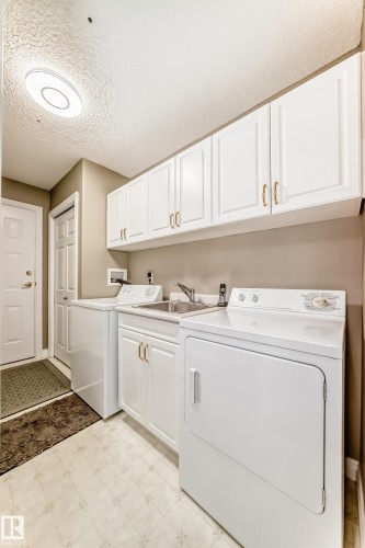 Functional laundry space featuring white cabinetry, a utility sink, and durable tile-patterned flooring - 29 929 Picard Drive, Edmonton, AB - Indoor Photo Showing Laundry Room