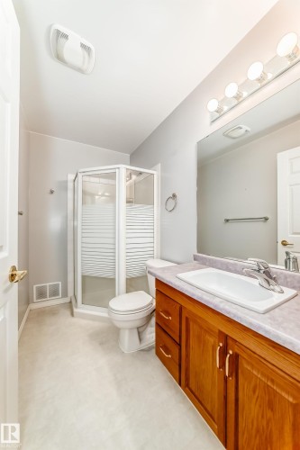 Bathroom featuring a wood-finish vanity with an integrated sink, a rectangular mirror, and a four-bulb vanity light fixture - 29 929 Picard Drive, Edmonton, AB - Indoor Photo Showing Bathroom