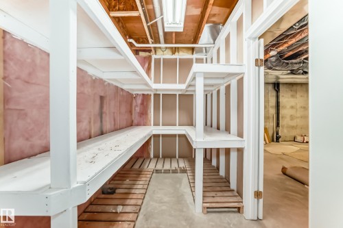 Unfinished basement storage area featuring extensive built-in shelving, exposed joists, concrete flooring, and a visible utility area - 29 929 Picard Drive, Edmonton, AB - Indoor Photo Showing Other Room