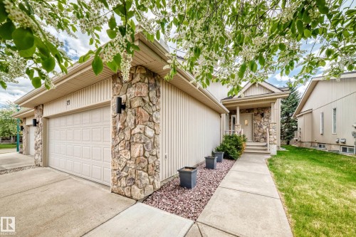 Stone veneer accents on the facade, a paneled garage door, a covered front entry, and a concrete walkway - 29 929 Picard Drive, Edmonton, AB - Outdoor