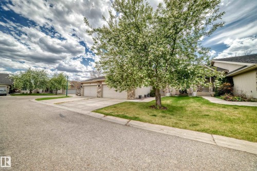 Front exterior featuring a multi-car driveway, attached garage, stone accents, and mature trees - 29 929 Picard Drive, Edmonton, AB - Outdoor