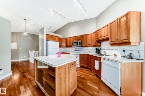 Kitchen featuring warm wood cabinetry, white countertops, built-in appliances, a central island with integrated storage, and wood-finish flooring - 29 929 Picard Drive, Edmonton, AB - Indoor Photo Showing Kitchen