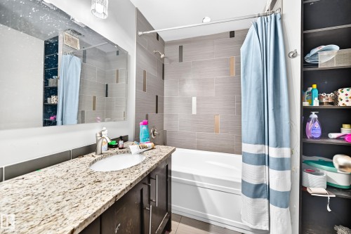 Bathroom featuring a built-in tub with shower, tiled surround with accent strips, vanity with granite countertop, and integrated shelving - 199 Westridge Road, Edmonton, AB 