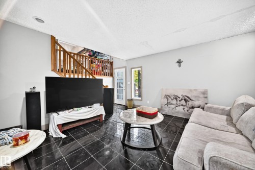 Spacious living area featuring dark tile flooring, a wood staircase with balusters, and light gray walls - 199 Westridge Road, Edmonton, AB 
