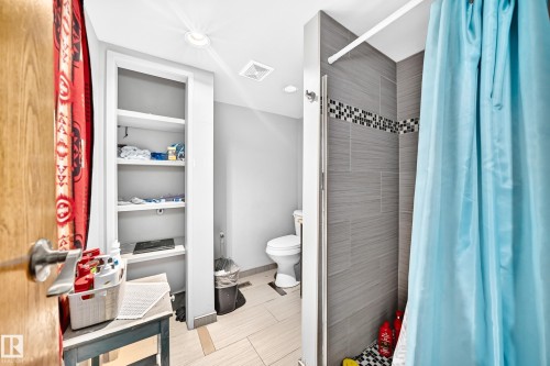 Bathroom featuring a tiled shower with mosaic accent, built-in shelving, recessed lighting, and a white toilet - 199 Westridge Road, Edmonton, AB 