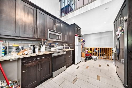 Kitchen featuring dark wood cabinetry, stainless steel appliances, light-toned patterned tile flooring, a subway tile backsplash, and stone-finish countertops - 199 Westridge Road, Edmonton, AB 