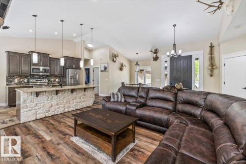 Open-concept living space featuring vaulted ceilings, wood-finish flooring, a kitchen island with stone detailing and pendant lighting, and dark wood cabinetry with stainless steel appliances - #6 2406 Twp Road 540, Rural Lac Ste. Anne County, AB - Indoor Photo Showing Living Room