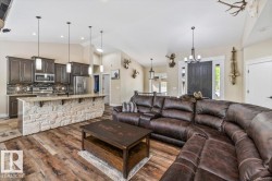Open-concept living space featuring vaulted ceilings, wood-finish flooring, a kitchen island with stone detailing and pendant lighting, and dark wood cabinetry with stainless steel appliances - 