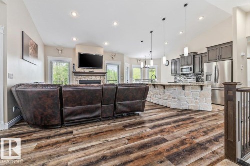 Open-concept living area featuring wood-finish flooring, a stone-faced kitchen island, dark wood cabinetry, and stainless steel appliances - #6 2406 Twp Road 540, Rural Lac Ste. Anne County, AB - Indoor With Fireplace