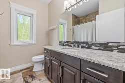 Bathroom featuring a dark wood-finish vanity with a light speckled countertop, dual under-mount sinks, and a horizontal mosaic tile backsplash - 