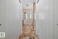 Hallway featuring board-and-batten style closet doors, varied-tone stone tile flooring, and a built-in shelving unit - 