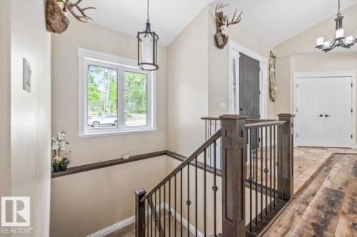 Entryway featuring a wood-finish staircase with wrought iron balusters, a rectangular window with white trim, a dark wood-paneled door, and a white paneled door - #6 2406 Twp Road 540, Rural Lac Ste. Anne County, AB - Indoor Photo Showing Other Room