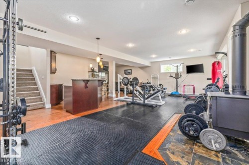Spacious lower level featuring a dedicated fitness area with rubber mat flooring, a built-in bar with pendant lighting, wood-finish flooring, a carpeted staircase, and recessed ceiling lights - #6 2406 Twp Road 540, Rural Lac Ste. Anne County, AB - Indoor Photo Showing Gym Room