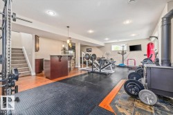 Spacious lower level featuring a dedicated fitness area with rubber mat flooring, a built-in bar with pendant lighting, wood-finish flooring, a carpeted staircase, and recessed ceiling lights - 