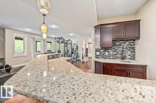 Expansive stone-finish countertop bar with a built-in sink and dark wood-finish cabinetry - #6 2406 Twp Road 540, Rural Lac Ste. Anne County, AB - Indoor Photo Showing Kitchen