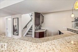 Expansive granite countertop bar area featuring a built-in wet bar with dark wood cabinetry, a contemporary black faucet, and a mosaic tile backsplash - 