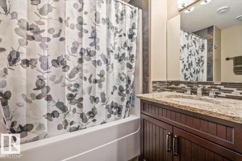 Bathroom featuring a built-in bathtub with tiled surround, a vanity with a granite-finish countertop, an undermount sink, and a framed mirror - #6 2406 Twp Road 540, Rural Lac Ste. Anne County, AB - Indoor Photo Showing Bathroom
