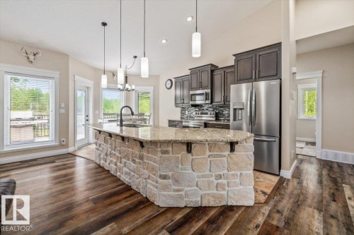 Spacious kitchen featuring a stone-clad island with a granite-style countertop, stainless steel appliances, dark wood cabinetry, and wood-finish flooring - #6 2406 Twp Road 540, Rural Lac Ste. Anne County, AB - Indoor Photo Showing Kitchen With Upgraded Kitchen