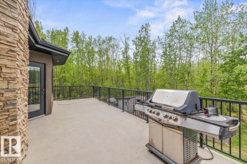 Expansive exterior deck featuring a stone facade, glass-paneled door, and black metal railing, surrounded by mature trees - #6 2406 Twp Road 540, Rural Lac Ste. Anne County, AB - Outdoor With Exterior