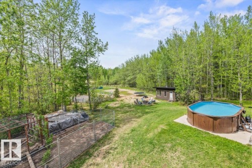 Expansive outdoor area featuring a wood-sided above-ground pool on a concrete pad, a small outbuilding with a single door and window, a fenced enclosure, and a gravel patio area - #6 2406 Twp Road 540, Rural Lac Ste. Anne County, AB - Outdoor With Above Ground Pool