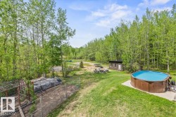 Expansive outdoor area featuring a wood-sided above-ground pool on a concrete pad, a small outbuilding with a single door and window, a fenced enclosure, and a gravel patio area - 