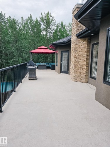 Expansive outdoor deck featuring a black metal railing, a stone-clad exterior element, and large windows with dark frames - #6 2406 Twp Road 540, Rural Lac Ste. Anne County, AB - Outdoor With Exterior