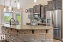 Kitchen featuring a stone-faced island with a granite-style countertop, stainless steel appliances, dark wood-finish cabinetry, a mosaic tile backsplash, and pendant lighting - #6 2406 Twp Road 540, Rural Lac Ste. Anne County, AB  - Indoor Photo Showing Kitchen With Double Sink With Upgraded Kitchen 