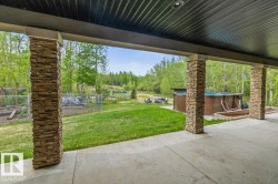 Expansive concrete patio area with stacked stone pillars, overlooking a large grassy yard and wooded terrain - 