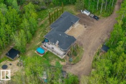 Sprawling property featuring a multi-level home with a large elevated deck, an oval above-ground swimming pool, and multiple outbuildings, all surrounded by mature trees - 