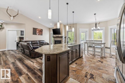 Open-concept living space featuring vaulted ceilings, wood-finish flooring, a stone-faced fireplace, a kitchen island with granite countertop, and natural light from multiple windows - #6 2406 Twp Road 540, Rural Lac Ste. Anne County, AB - Indoor Photo Showing Kitchen With Upgraded Kitchen