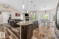 Open-concept living space featuring vaulted ceilings, wood-finish flooring, a stone-faced fireplace, a kitchen island with granite countertop, and natural light from multiple windows - 
