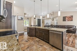 Open-concept kitchen featuring an expansive island with a built-in sink, granite countertops, and dark wood cabinetry - 