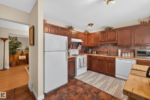 Kitchen featuring wood cabinetry, white appliances, a brick-style tile backsplash, and tile flooring - 12062 157 Avenue, Edmonton, AB 