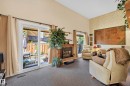 Spacious living area featuring a fireplace with a stone surround, a high vaulted ceiling, and sliding glass doors leading to an outdoor patio with privacy fencing - 12062 157 Avenue, Edmonton, AB 