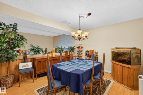 Dining area featuring wood-finish flooring, a brass-toned chandelier with frosted glass shades, and light-toned wall paint - 12062 157 Avenue, Edmonton, AB 