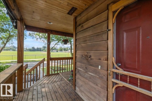 Expansive wooden front porch with a red entry door and screen door - 11603 70 Street Nw, Edmonton, AB 