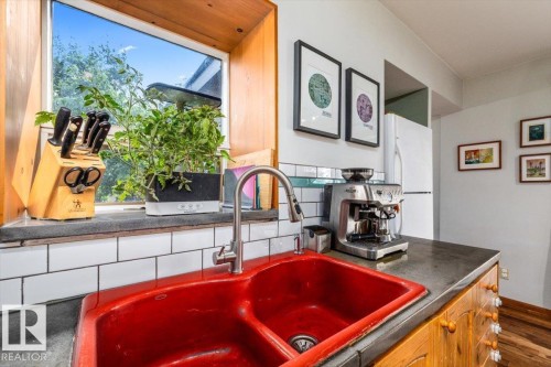 Kitchen featuring a vibrant red double basin sink with a pull-down faucet, a white subway tile backsplash, and wood-finish cabinetry - 11603 70 Street Nw, Edmonton, AB 