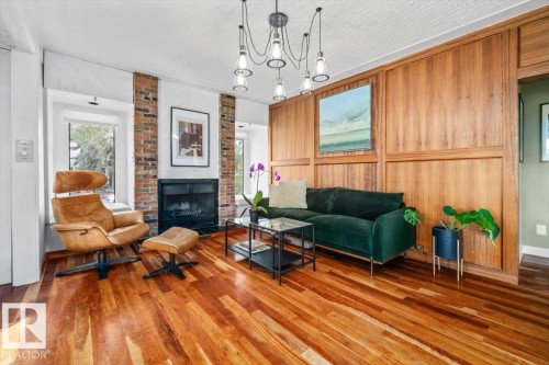 Living area featuring wood-finish flooring, a brick fireplace, paneled wood wall accents, and an overhead multi-bulb light fixture - 11603 70 Street Nw, Edmonton, AB 