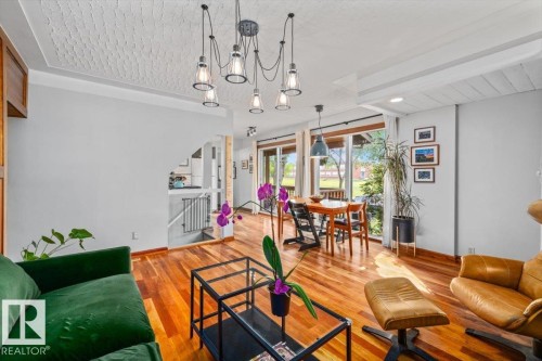 Open-concept living space featuring wood-finish flooring, a contemporary multi-bulb chandelier, large sliding glass doors, and a dining area - 11603 70 Street Nw, Edmonton, AB 