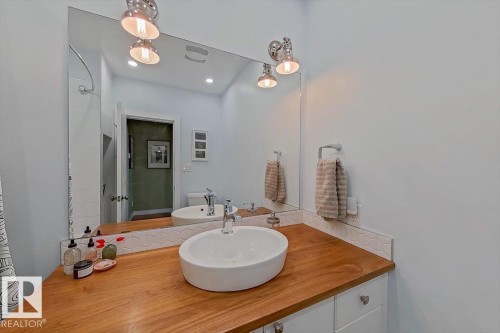 Bathroom vanity featuring a vessel sink, wood-finish countertop, and white cabinetry with brushed nickel hardware - 11603 70 Street Nw, Edmonton, AB 