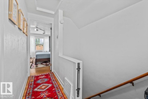 Hallway with wood-finish flooring, white painted walls, a wood handrail, and built-in lighting fixtures - 11603 70 Street Nw, Edmonton, AB 