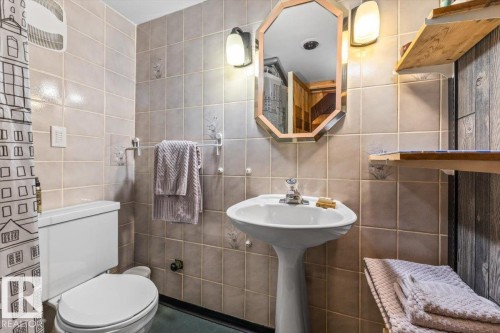 Pedestal sink with chrome faucet, octagonal mirror, wall-mounted light fixtures, and tiled walls - 11603 70 Street Nw, Edmonton, AB 