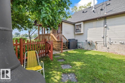 Grassy backyard featuring a wooden picket fence, a wood deck with stairs, a bay window, and stone pathway - 11603 70 Street Nw, Edmonton, AB 