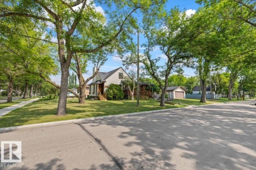 Charming home featuring a pitched roof, front porch, mature trees, manicured lawn, and a detached garage - 11603 70 Street Nw, Edmonton, AB 