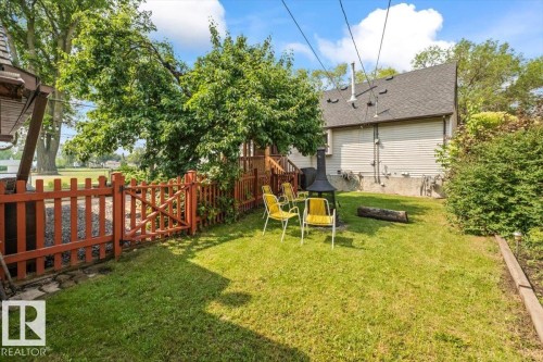 Grassed backyard featuring a wooden picket fence, mature trees, a raised garden bed, and a partial view of the property's exterior siding - 11603 70 Street Nw, Edmonton, AB 
