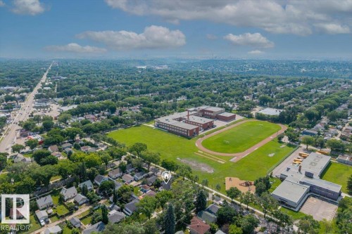 Aerial perspective showcasing a residential neighborhood with extensive tree canopies, featuring a prominent school building with athletic fields and a track - 11603 70 Street Nw, Edmonton, AB 