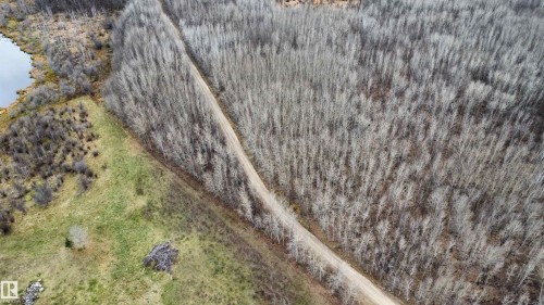 Expansive natural landscape featuring a dirt road, mature deciduous forest, open grassy areas, and a visible body of water - Rge Rd 62, Rural Barrhead County, AB 